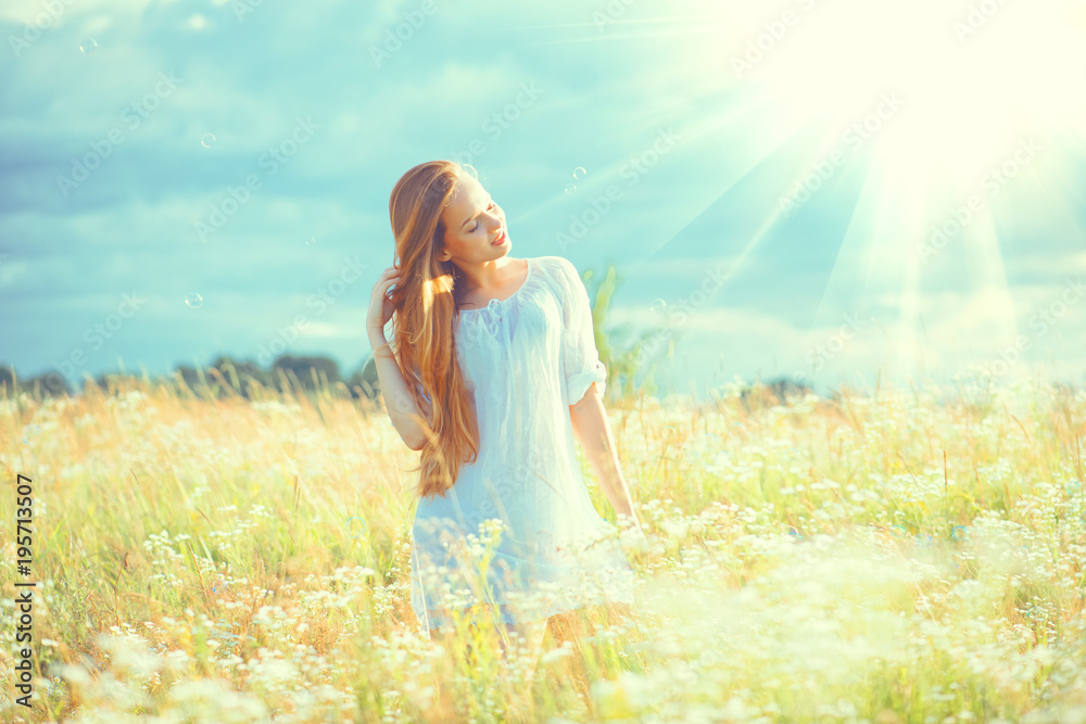 Naklejka premium Beauty girl outdoors enjoying nature. Beautiful teenage model girl with healthy long hair in white dress standing on the summer field
