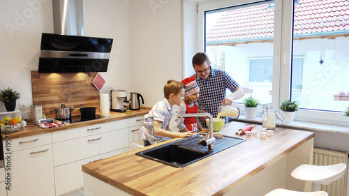 Young father with two happy children backing cookies in modern kitchen