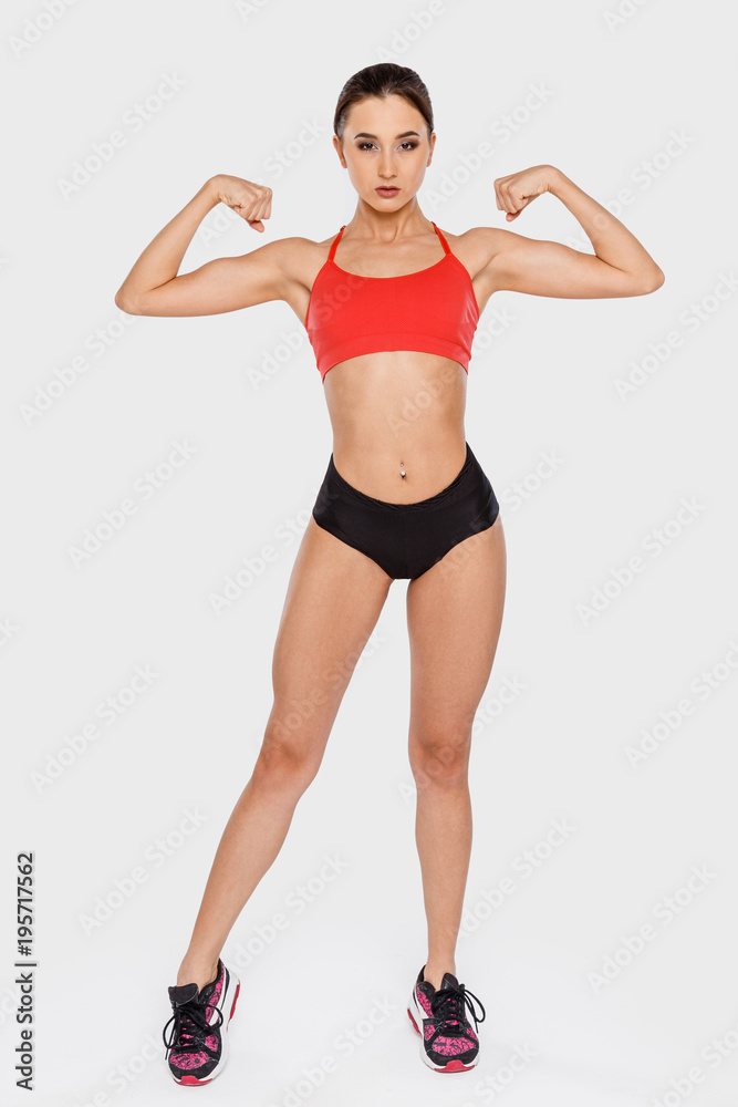 A strong young woman demonstrates her hands muscles standing on a gray background A strong young woman demonstrates her hands muscles standing on a gray background