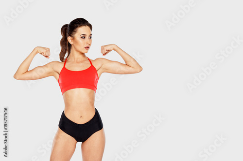 Strong girl showing biceps standing on light background