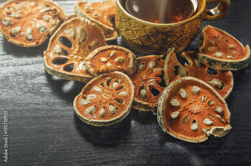 Dried herbs and dried bael fruit, Close-up of bael dry and glass tea and bael juice on the wooden floor, Slices of bael fruit on the dark table.