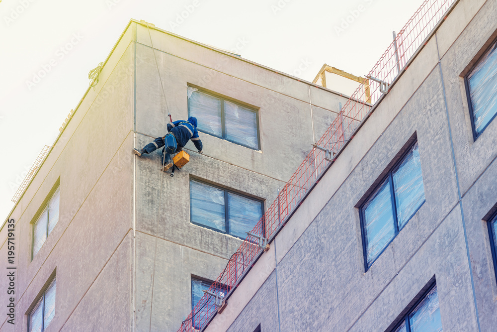Industrial climber on the wall of the house under construction, makes the sealing of seams between concrete panels Industrial climber on the wall of the house under construction, makes the sealing of seams between concrete panels