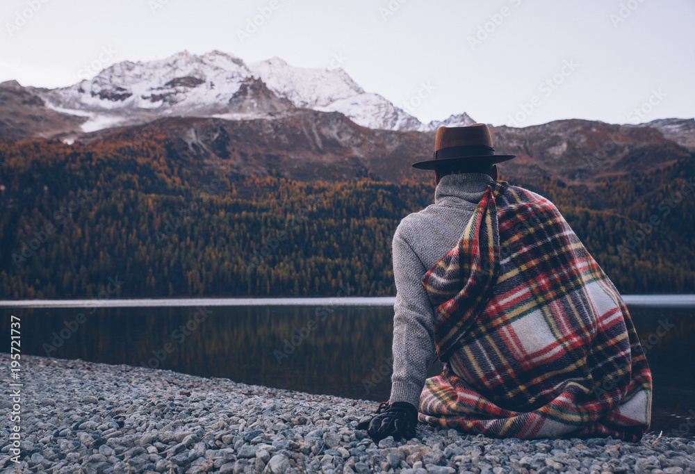 Lonely man enjoying sunrise on a lake beach with mountains background