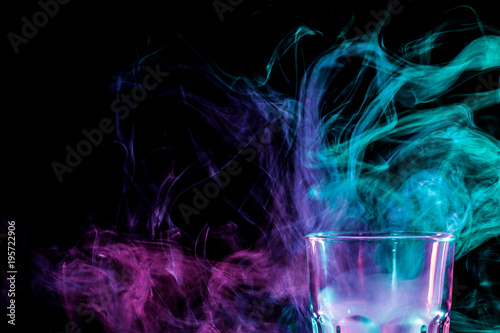 Close up of a new glass with soft multi-colored purple and green smoke from vape on a black isolated background