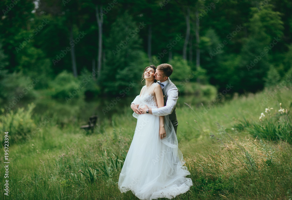 Bride and groom walking and holding hands on a meadow. Wide angle sunset photo.