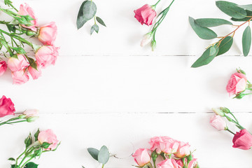 Flowers composition. Frame made of eucalyptus branches and pink rose flowers on white wooden background. Flat lay, top view, copy space