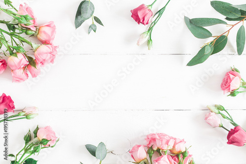 Flowers composition. Frame made of eucalyptus branches and pink rose flowers on white wooden background. Flat lay, top view, copy space