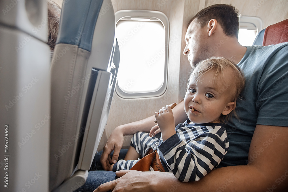 Fototapeta premium Man with little adorable boy on knees sitting near window in plane flying. 