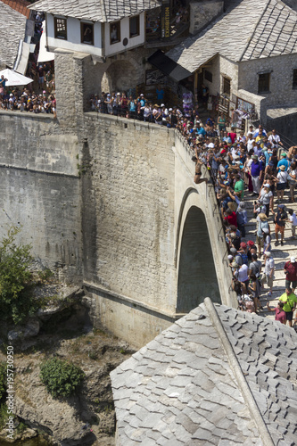 Person diving from the old bridge of Mostar, surrounded by a crowd of people