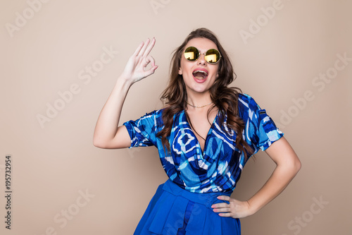 Beautiful cheerful summer young woman in sunglasses standing over a color background