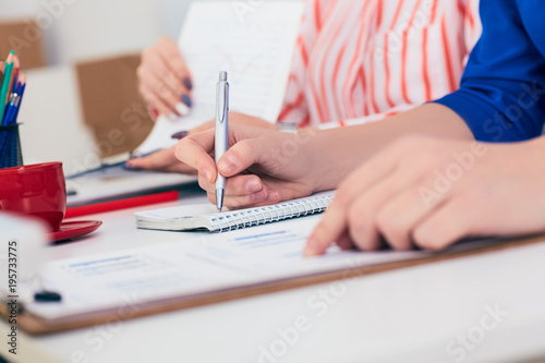 Two female business workers discussing graphs at office. Just hands over the table.