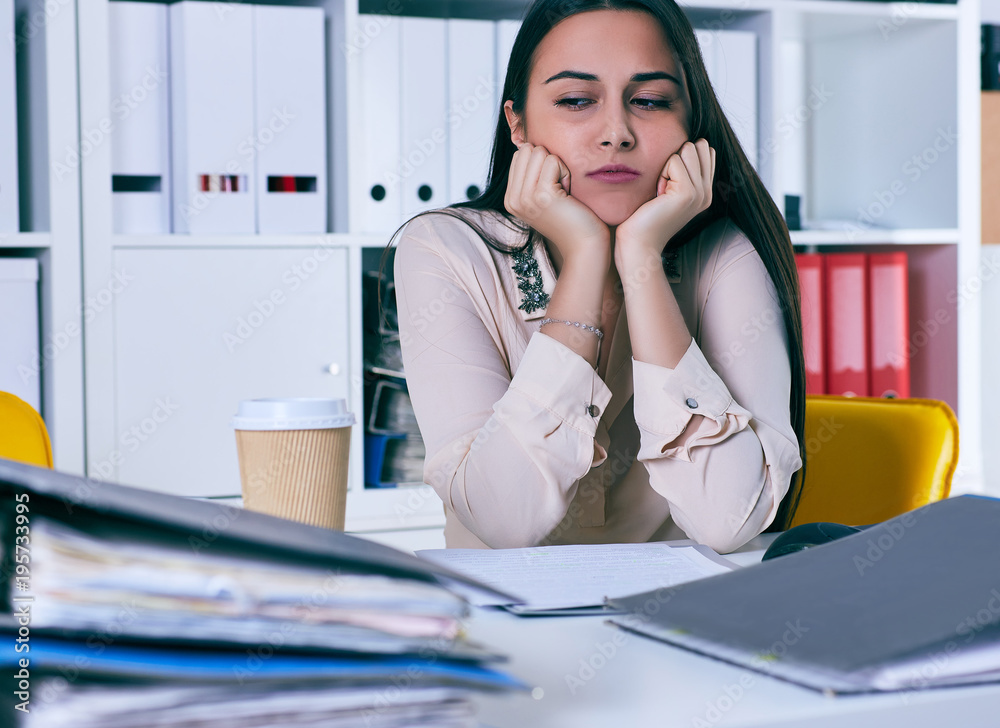 Tired and exhausted woman looks at the mountain of documents propping up her head with her hands. Tired and exhausted woman looks at the mountain of documents propping up her head with her hands.