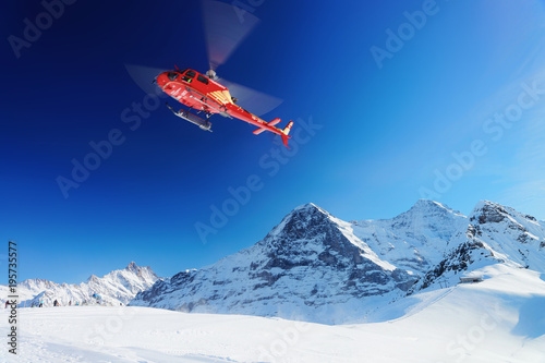 Red helicopter flying Swiss Alpine mountain Mannlichen in winter