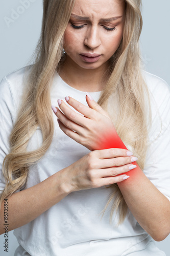 Young Caucasian woman holding her painful wrist caused by prolonged work on computer, laptop. Carpal tunnel syndrome, arthritis, neurological disease concept