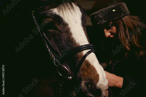 young woman rider engaged since a horse in the stables, prepare for departure