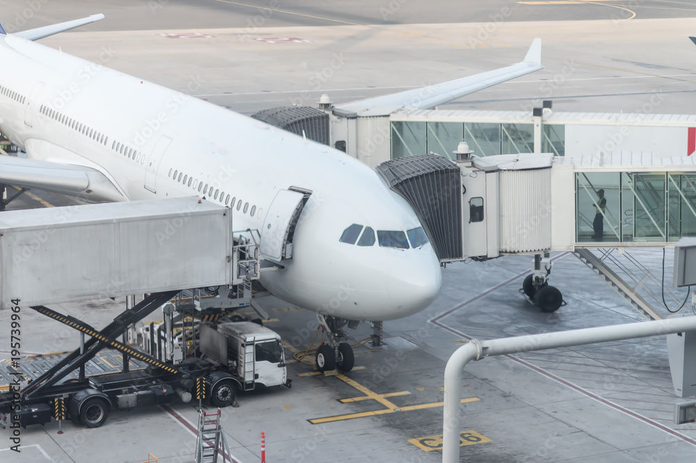Airplain docked to a jetway at airport. A Jet bridge. Loading and unloading of cargoes by special equipmen Airplain docked to a jetway at airport. A Jet bridge. Loading and unloading of cargoes by special equipmen