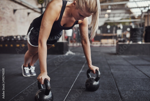 Fit young woman doing pushups with weights in a gym