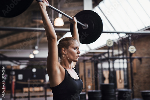 Young woman lifting weights over her head in a gym