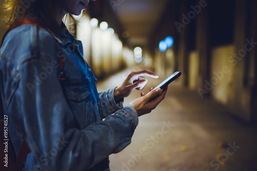 Woman pointing finger on blank screen smartphone on background bokeh light in night atmospheric city, hipster blogger using in hands clean gadget mobile phone, mockup online wifi internet concept