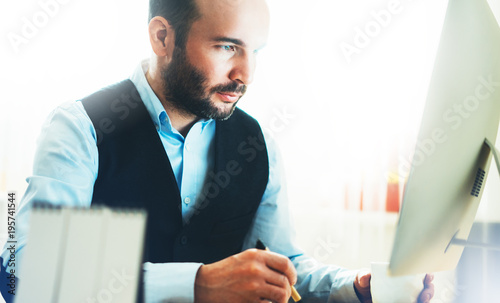 Bearded young businessman working on modern office. Consultant man thinking looking in monitor computer. Manager typing on keyboard in coworking workplace photo