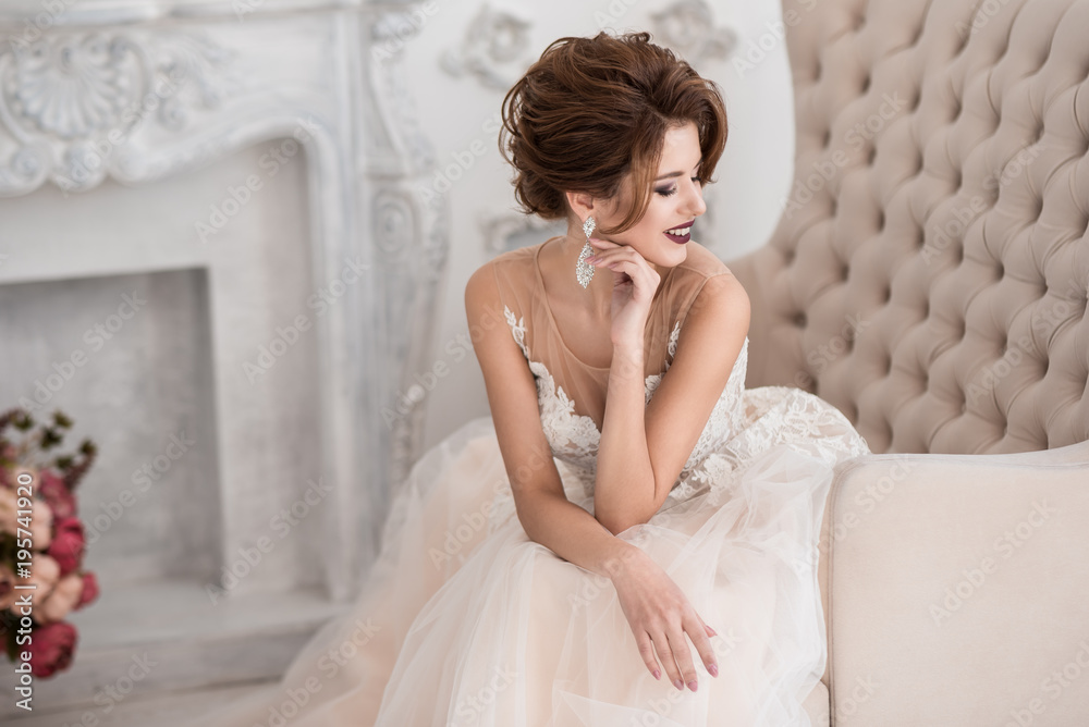 Beautiful bride sitting on the couch. Wedding hairstyle and makeup. Leaning his head on his arm. Lace dress. Beige sofa.