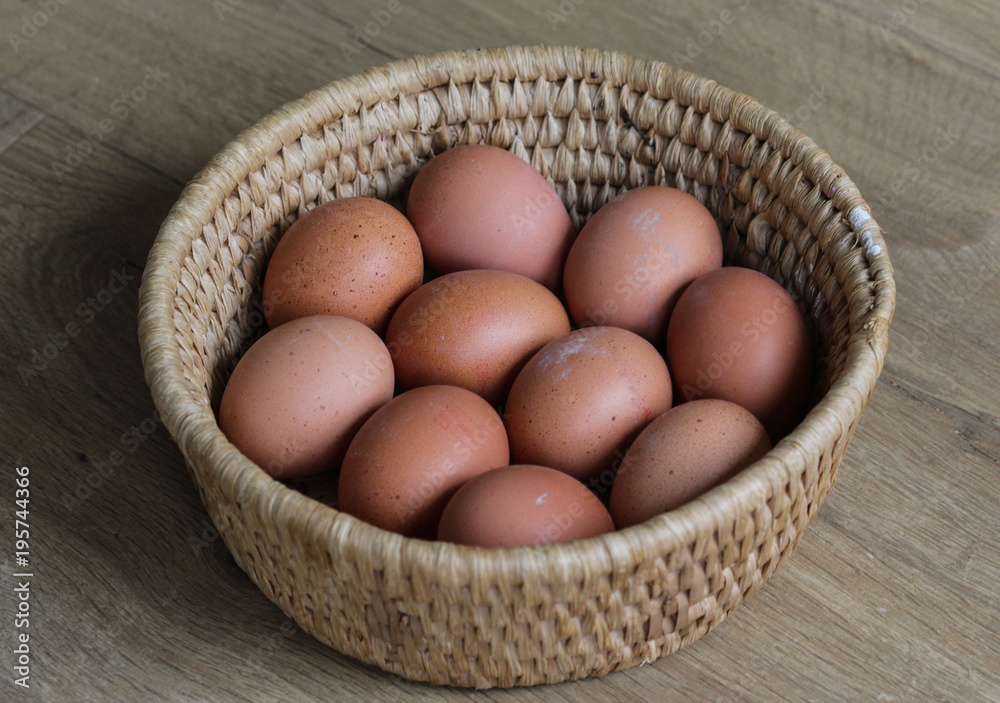 Brown chicken eggs in straw basket on wooden background in kitchen Brown chicken eggs in straw basket on wooden background in kitchen