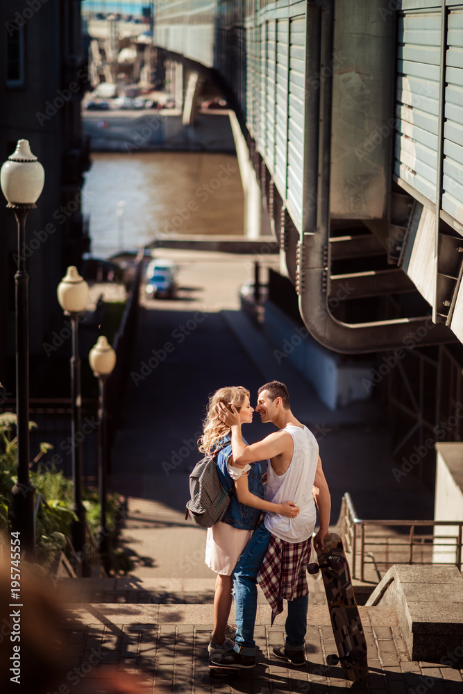 Street sport and hobby concept. Vertical shot of lovely couple of skaters have break after skating, embrace and going to kiss, enjoy togetherness and love. Active lifestyle and relationship concept.