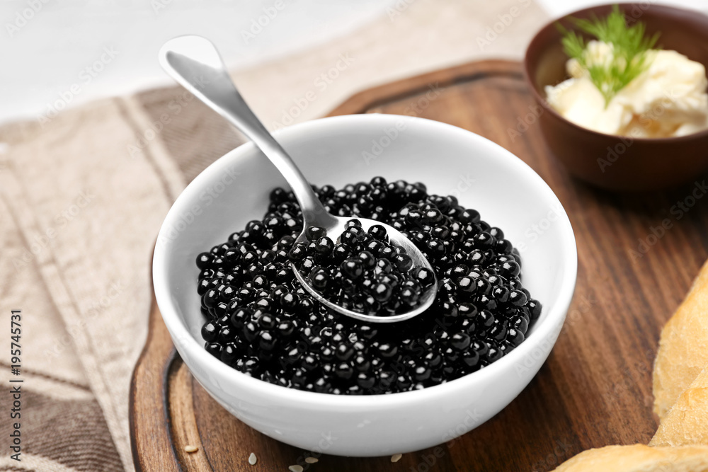 Bowl and spoon with delicious black caviar on wooden board, closeup Bowl and spoon with delicious black caviar on wooden board, closeup