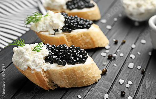 Sandwiches with delicious black caviar and cottage cheese on wooden board