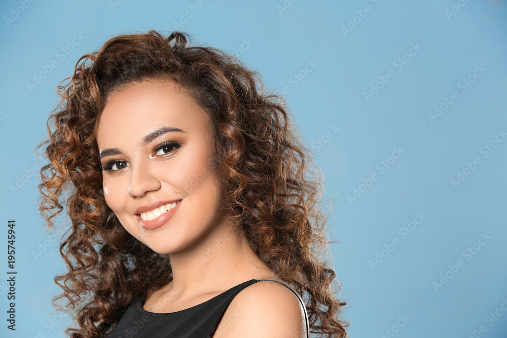 Beautiful young African American woman with long wavy hair on color background