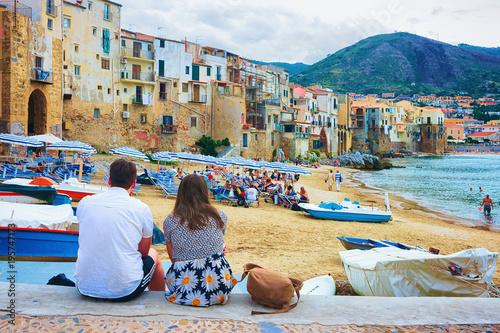 Fototapeta Naklejka Na Ścianę i Meble -  Young couple sitting at beach in Cefalu Sicily