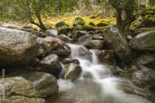view of a stream flowing down from stickle tarn in langdale in the lake district national park in the north of england showing the blurred water moving down over dark rock