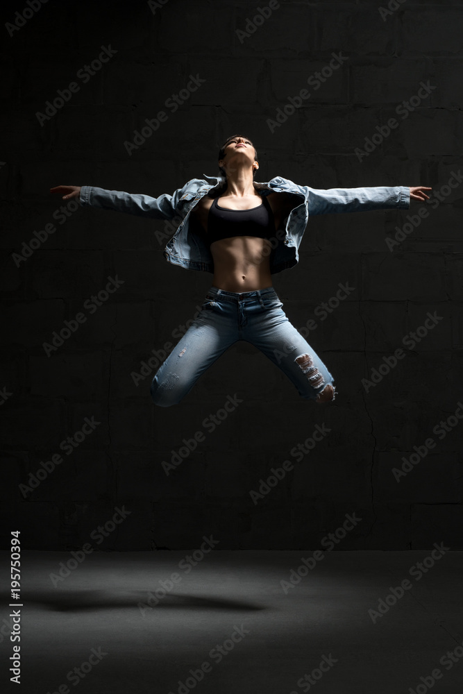 Ballet dancer in jeans jumping in dark room