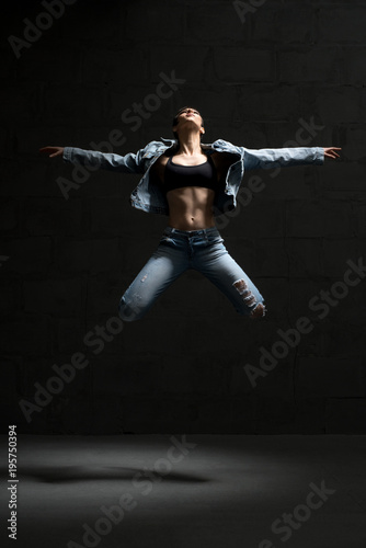 Ballet dancer in jeans jumping in dark room