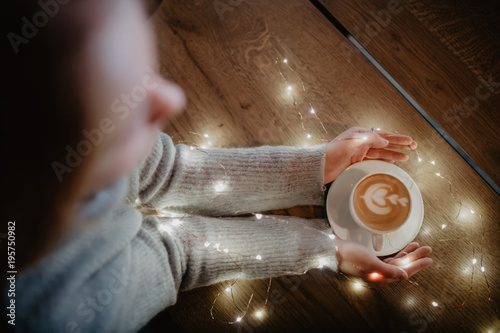 Girl holding coffee in hands over light bokeh background. Nice winter photo of hands with coffee cup with magic light. photo