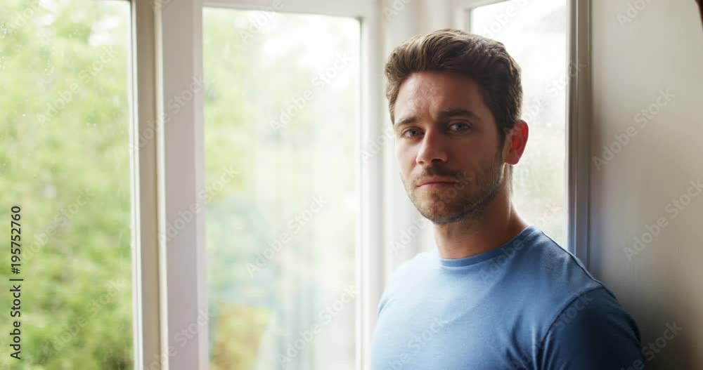 4K Man staring out of window turns to look at camera with a subtle smile. Slow motion.