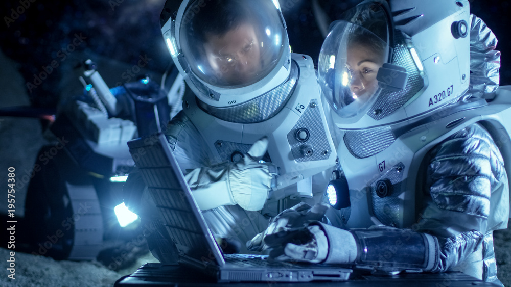 Two Astronauts Wearing Space Suits Work on a Laptop, Exploring Newly