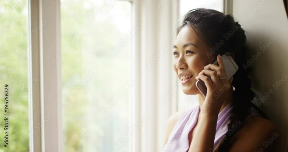 4K Cheerful woman standing next to window makes a call on cell phone as rain falls outside. Slow motion. 4K Cheerful woman standing next to window makes a call on cell phone as rain falls outside. Slow motion.