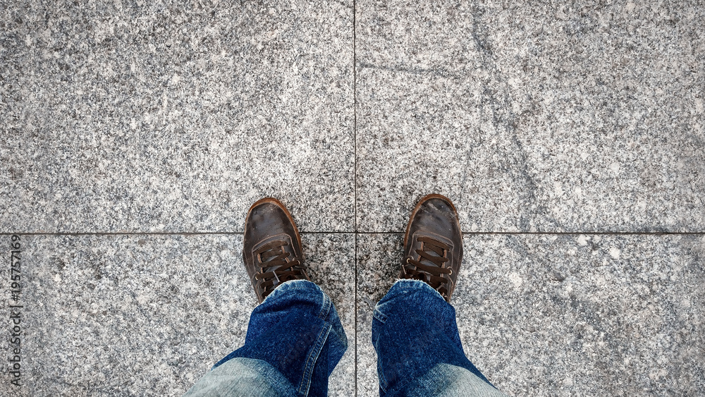 Old leather snakers and leg blue jeans top view on paving stone Old leather snakers and leg blue jeans top view on paving stone
