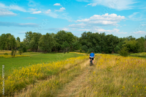 Young cyclist riding bicycle through green meadow against beautiful sky. © NatalyLandar