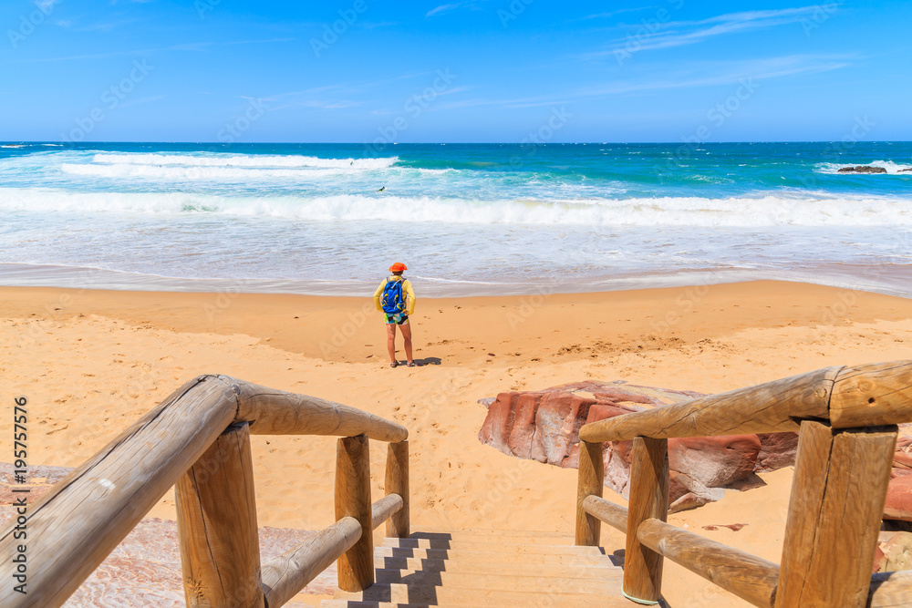 Φωτογραφία Walkway to sandy Praia do Amado beach and young woman tourist standing on sea sh