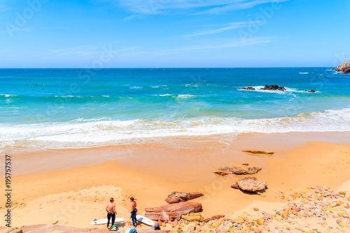 PRAIA DO AMADO BEACH, PORTUGAL - MAY 15, 2015: Surfers relaxing on Praia do Amado beach with ocean waves hitting shore. Algarve region is popular holiday destination in southern Europe.