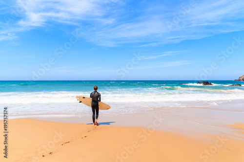PRAIA DO AMADO BEACH, PORTUGAL - MAY 15, 2015: Surfer walking on Praia do Amado beach with ocean waves hitting shore. Algarve region is popular holiday destination in southern Europe.