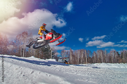 Sports race snowmobiles. Snowmobile in  high jump above track. Sportsman on snowmobile. Winter competition, sunny day, blue sky. Copy space. photo