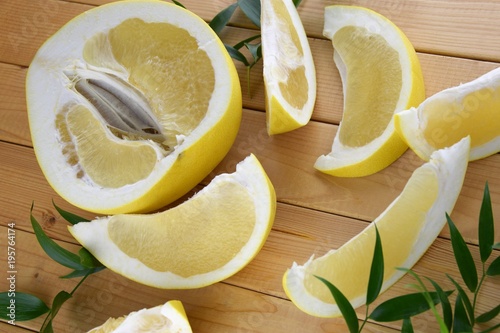 A half of pomelo and it's cut pieces on wooden background with green leafs, cut pomelo close up