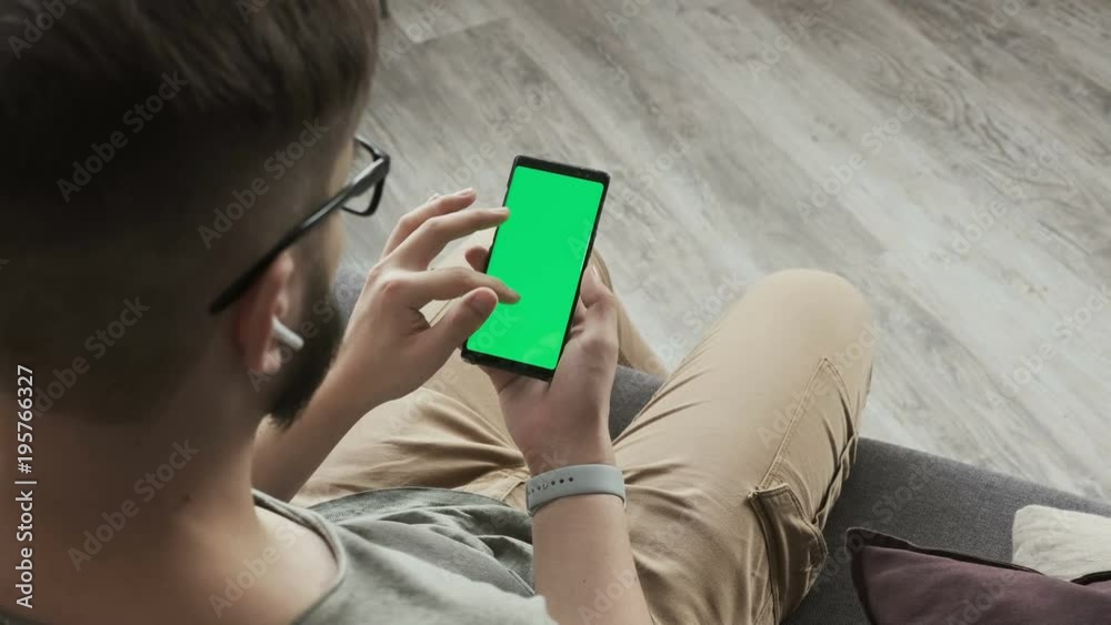 Man using smartphone with touching screen for internet surfing on-line and e-mail reading. Closeup of a male's hand holding a mobile telephone with a vertical green screen. Natural lighting Man using smartphone with touching screen for internet surfing on-line and e-mail reading. Closeup of a male's hand holding a mobile telephone with a vertical green screen. Natural lighting