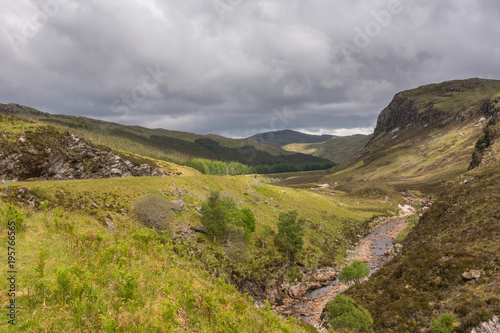 Braemore, Scotland - June 8, 2012: Dundonnell Rvier along A832 road offers bronwn rocks and grassy hills under dark cloudscape. Hills in back.  photo