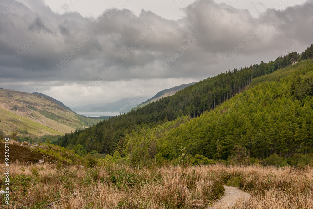 Braemore, Scotland - June 8, 2012: West of Corrieshalloch Gorge along A832 from height look upon Loch Broom under monumental cloudscape. Green forested mountains. Meadows on slopes and valley.