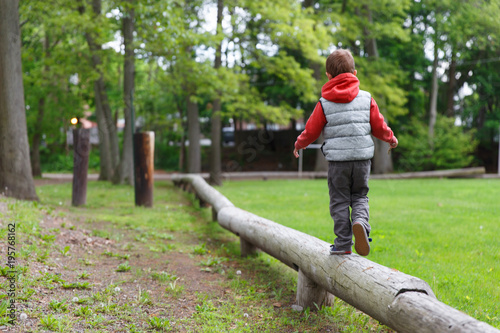 little child on the balance beam. boy walking on a log in the park. Back view. Copy space for your text photo