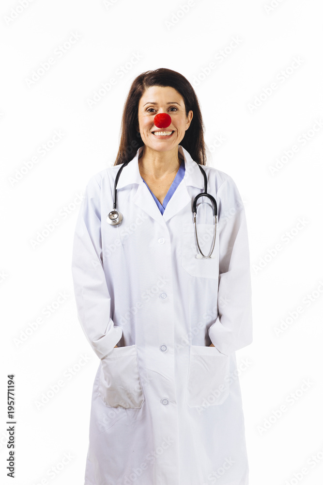 Portrait of a smiling female doctor with a red clown nose and arms in pockets, isolated on white background